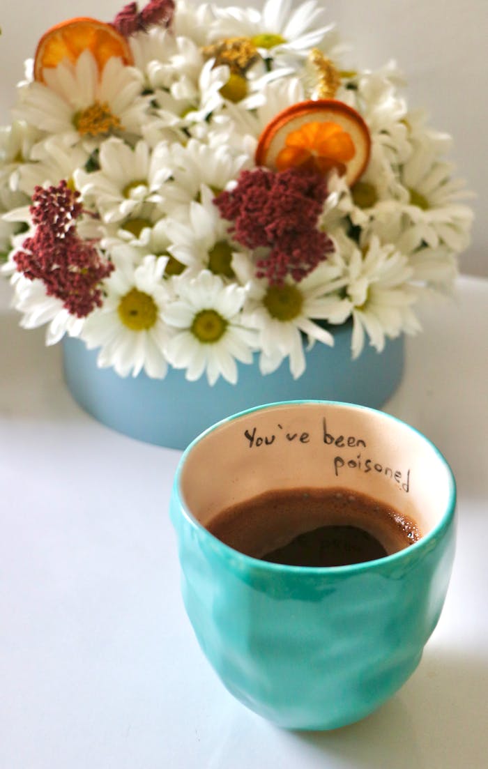 A quirky coffee cup with a humorous "You've been poisoned" message, set against a floral background.